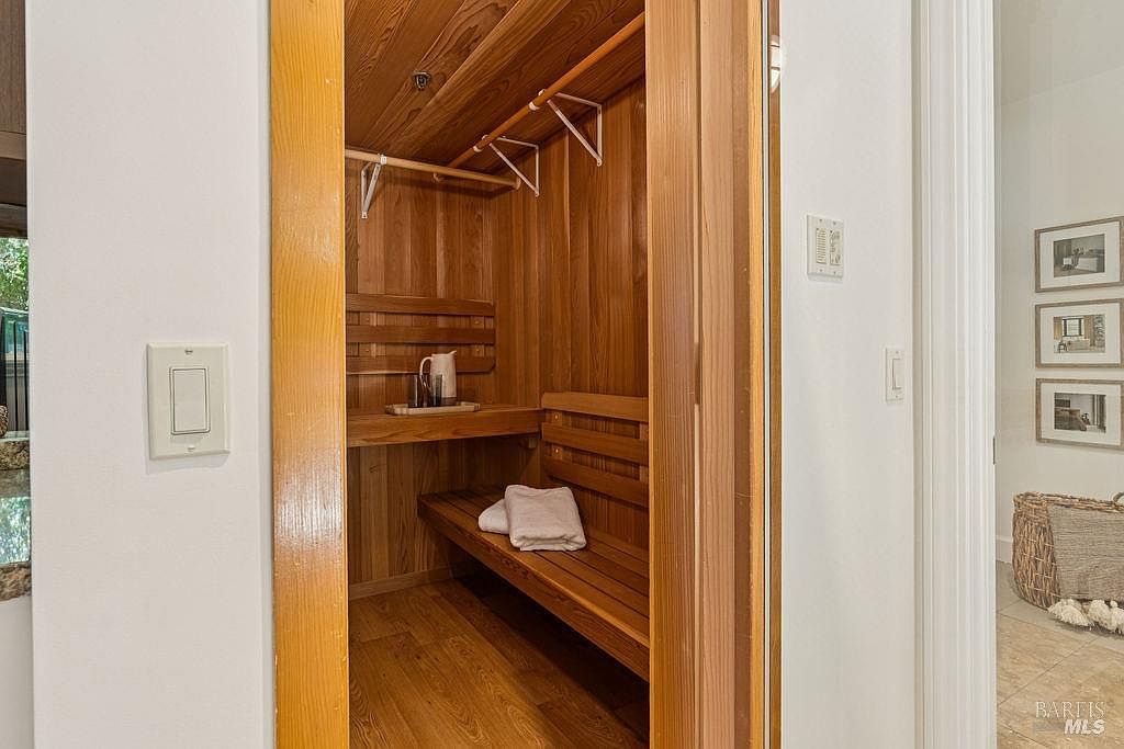 This image showcases a sauna located within a bathroom. The sauna features wooden benches and walls, creating a warm and inviting atmosphere. A pitcher and glasses sit on a shelf, and a neatly folded towel rests on the bench, suggesting a relaxing and luxurious experience.