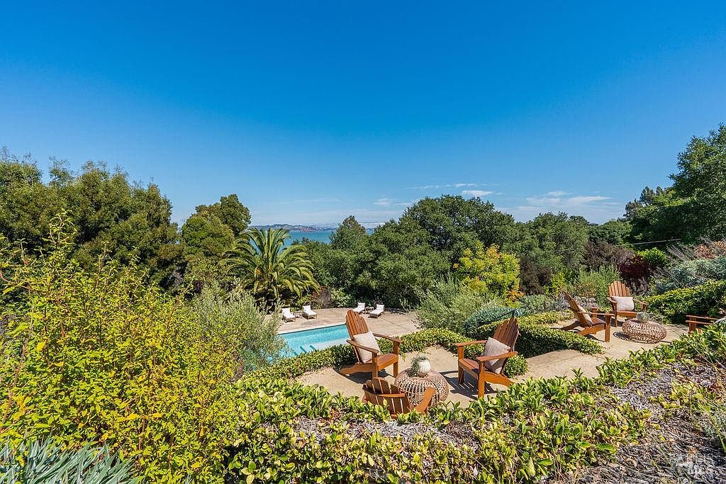 This image showcases a luxurious outdoor pool area with a stunning view. The pool is surrounded by lush greenery and a patio area furnished with comfortable seating, including Adirondack chairs. The scene evokes a sense of relaxation and upscale outdoor living, perfect for entertaining or enjoying a peaceful retreat.