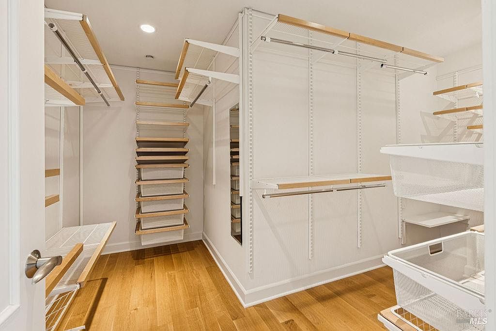 This is a well-organized walk-in closet featuring a custom shelving system with a combination of hanging rods, shelves, and pull-out drawers. The closet is brightly lit and has hardwood flooring, creating a clean and functional space for clothing and storage. The perspective is from the doorway, showcasing the depth and organization of the closet.