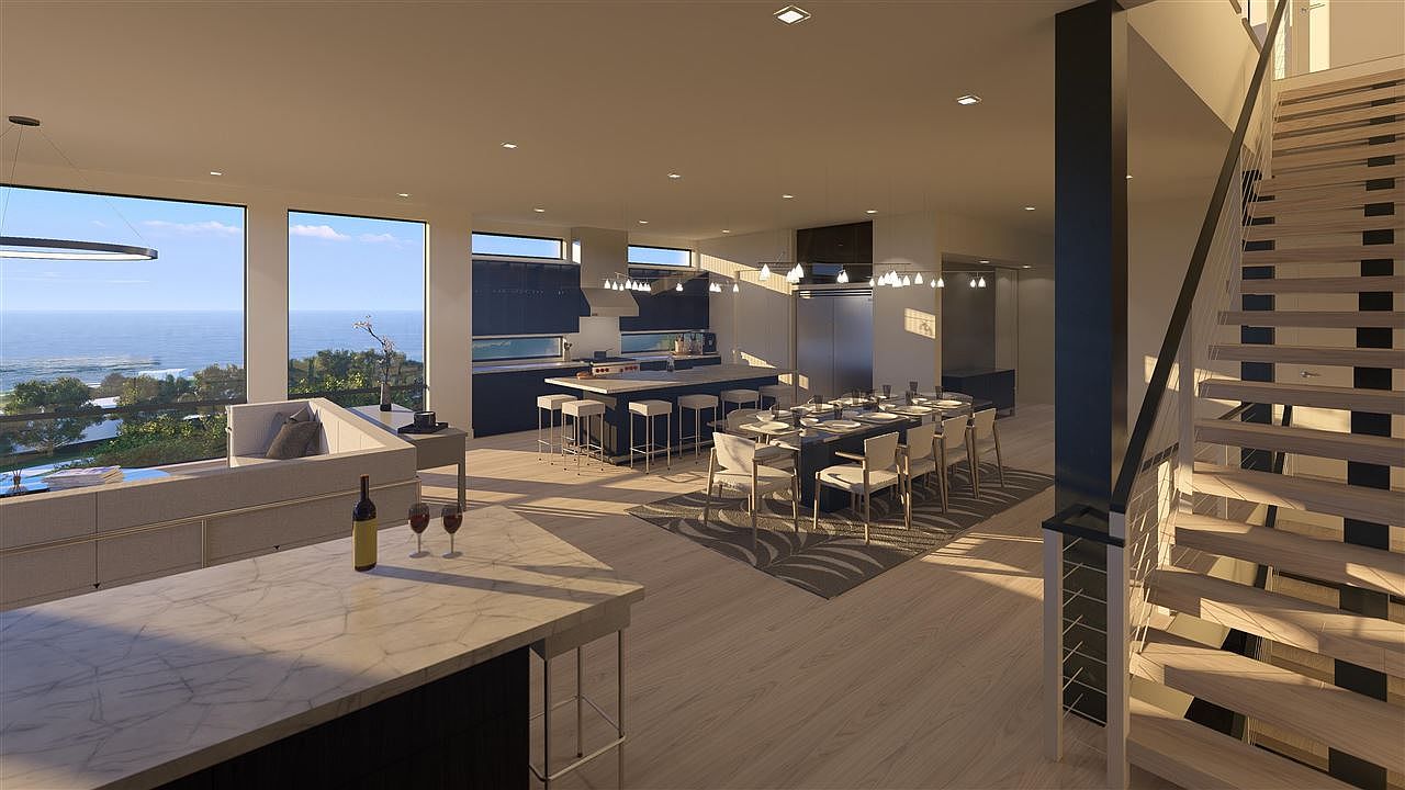 This is an interior shot of a modern living space that seamlessly integrates the kitchen and dining areas. The open floor plan features large windows with ocean views, a sleek kitchen island with bar seating, and a dining table set for a meal. A staircase is visible on the right, and the overall design emphasizes clean lines and natural light, creating a luxurious and inviting atmosphere.