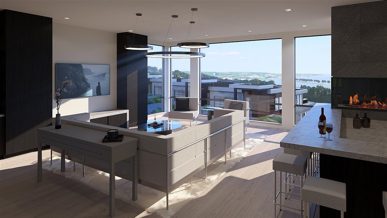 This is a modern living room featuring a sleek design with a neutral color palette. The room includes a large sectional sofa, a contemporary fireplace, and floor-to-ceiling windows offering a scenic view. The space is illuminated by modern pendant lighting, creating a sophisticated and inviting atmosphere.