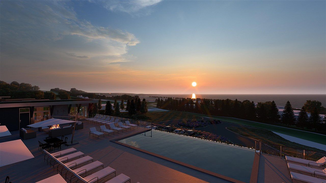 This image showcases a luxurious outdoor pool area at sunset, featuring modern lounge chairs, a fire pit, and a sleek building design. The infinity pool overlooks a scenic landscape with trees and the ocean, creating a serene and upscale ambiance. The overall impression is one of relaxation and high-end living.
