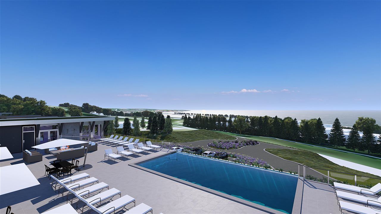 This image showcases a luxurious outdoor pool area with numerous lounge chairs, a modern outdoor seating area with a fire pit, and a sleek building in the background. The pool overlooks a beautifully landscaped area with trees and a glimpse of the ocean in the distance, creating a serene and upscale atmosphere. The scene suggests a high-end resort or private residence with premium amenities.