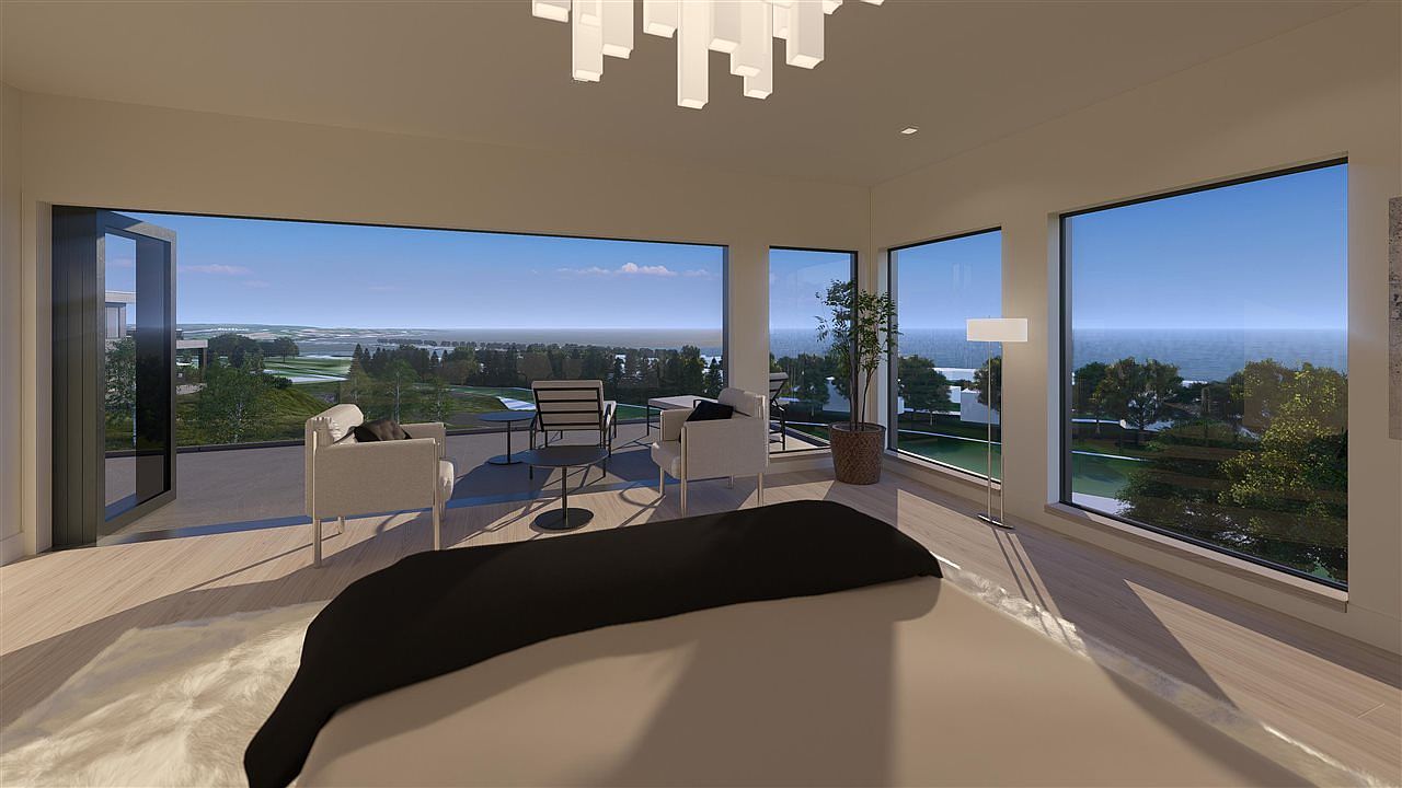 This is a luxurious primary bedroom with floor-to-ceiling windows offering stunning views of the landscape. The room features modern furniture, including chairs and a small table on the balcony, and a contemporary lighting fixture. The overall impression is one of spaciousness, elegance, and tranquility.