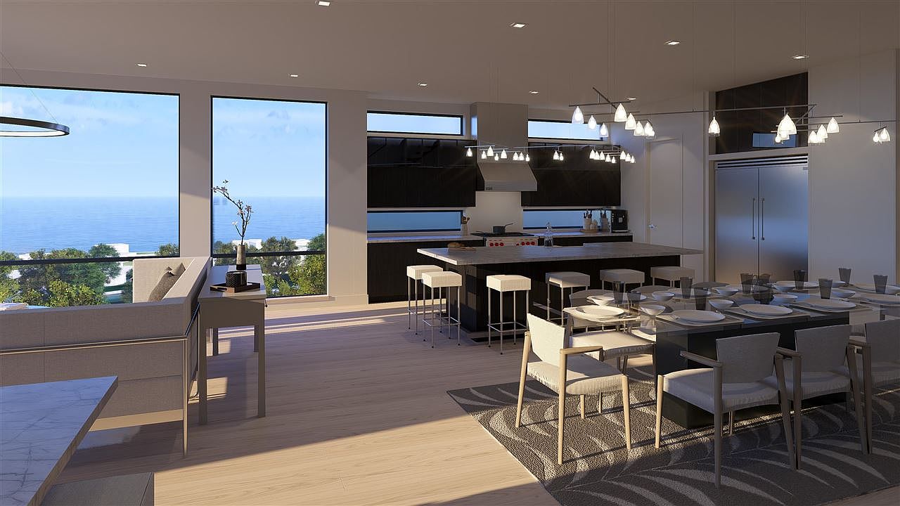This is a modern, open-concept kitchen and dining area with large windows offering ocean views. The kitchen features a large island with bar seating, sleek cabinetry, and stainless steel appliances. The dining area includes a long table set for a meal, with stylish chairs and a patterned rug, creating an inviting and luxurious atmosphere.