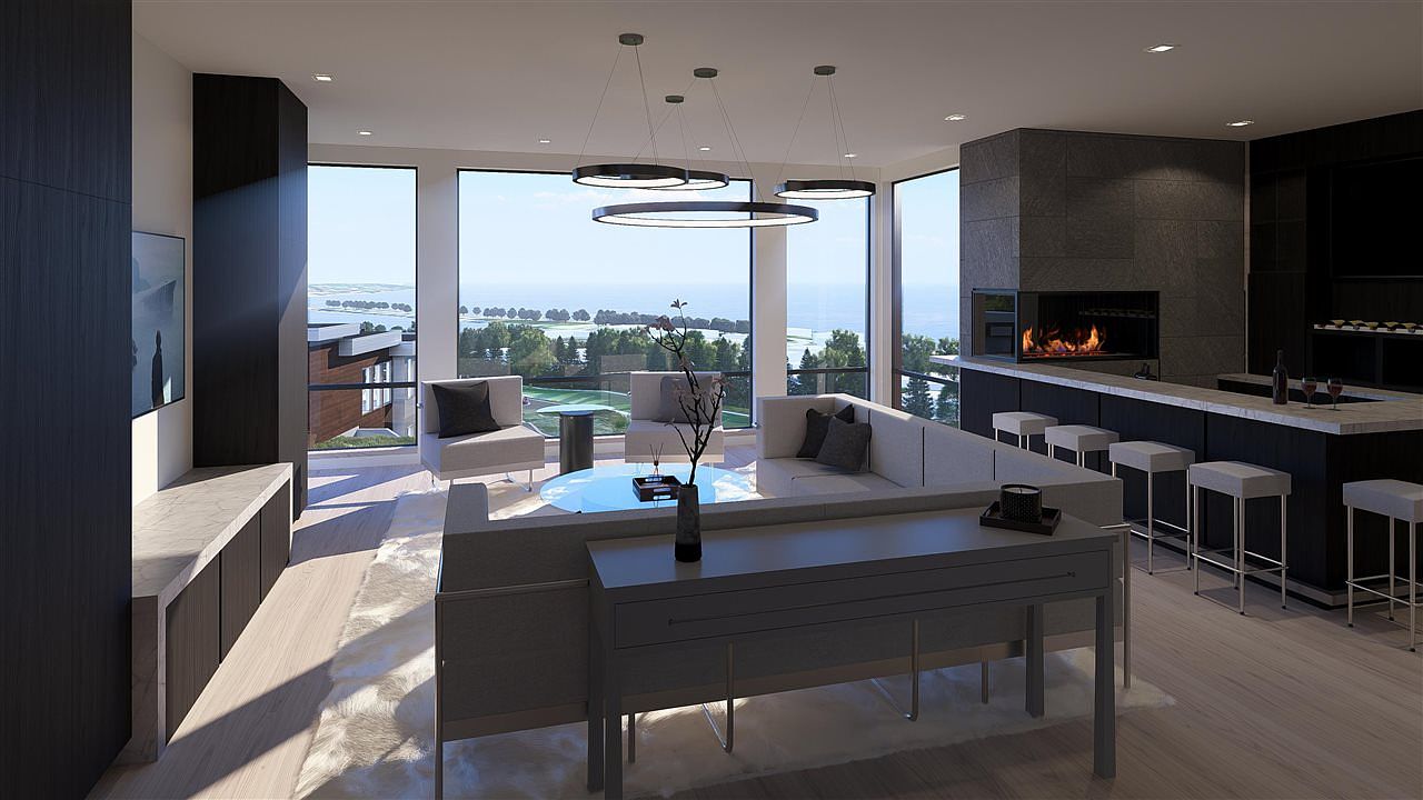 This is a modern living room featuring a sleek fireplace, a bar area with stools, and a comfortable seating arrangement with a view of the outdoors. The room is illuminated by contemporary circular pendant lights, and the color palette is neutral with dark accents, creating a sophisticated and inviting atmosphere. The perspective is from the front of the room, showcasing the entire space.