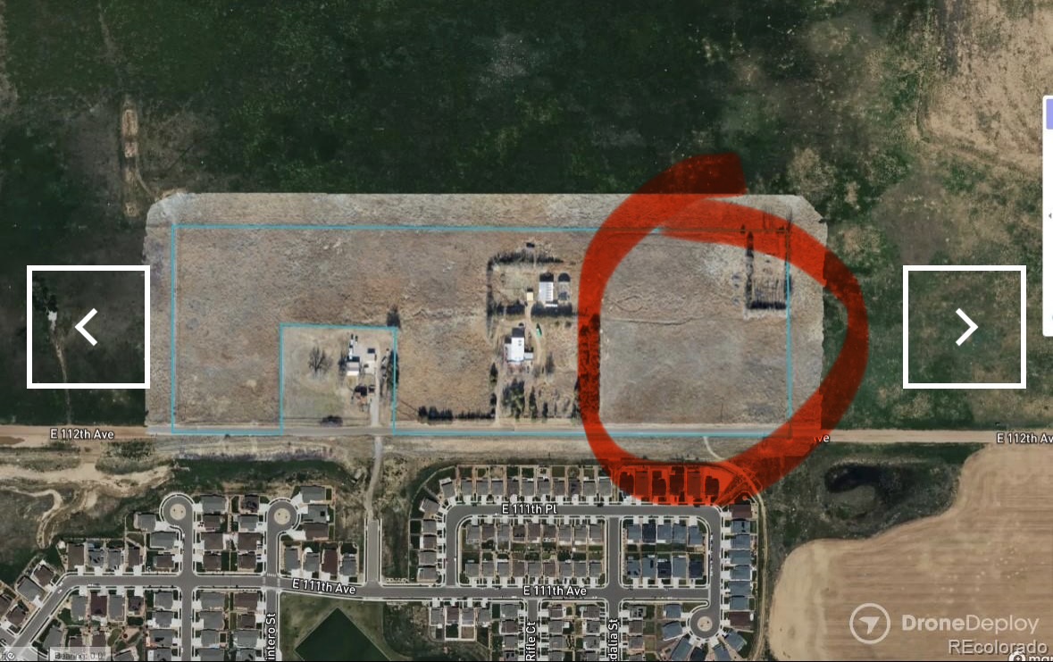 This aerial view captures a rectangular plot of land, featuring what appears to be a potential development site or large residential property. To the south, a new housing development is visible, contrasting with the open land. The image suggests potential for further development or a spacious property in a growing area.