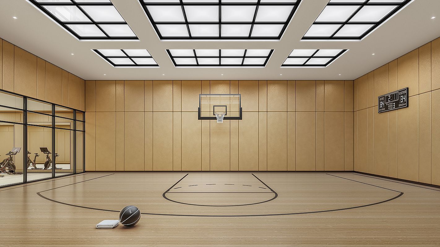 This indoor basketball court features light wood flooring and matching wood-paneled walls, creating a warm and cohesive aesthetic. A glass-enclosed gym area is visible to the left, while a digital scoreboard is mounted on the wall above the court. The space is illuminated by a grid of recessed ceiling panels, providing a bright and professional atmosphere.