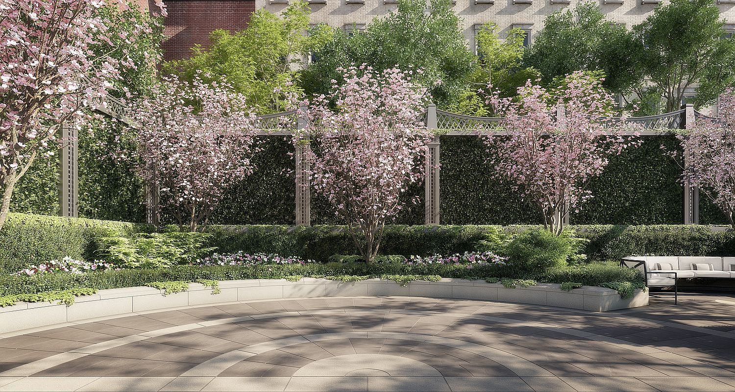 This serene outdoor garden space features a curved stone seating wall bordering a paved patio with a circular pattern. Several blooming pink trees are interspersed with lush green hedges and a decorative metal trellis structure, creating a private and tranquil atmosphere. The scene is captured from a ground-level perspective, emphasizing the elegant landscaping and the comfortable seating area tucked to the side.