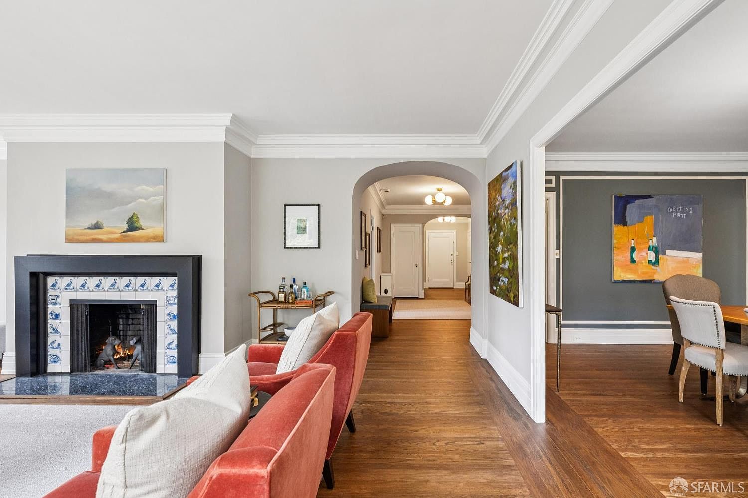 This interior shot showcases a living room with hardwood floors, a fireplace with decorative tiles, and comfortable seating. The room is painted in neutral tones, complemented by white trim and crown molding. Artwork adorns the walls, adding a touch of elegance to the space.