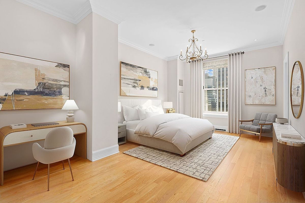 This elegant primary bedroom features a neutral color palette, light wood flooring, and a central bed dressed in crisp white linens. The room is accented by a crystal chandelier, abstract artwork, and a dedicated workspace with a modern desk and chair. Large windows with floor-length curtains allow natural light to fill the space, creating a bright and sophisticated atmosphere.