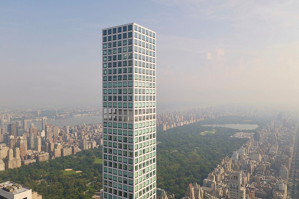 This aerial view showcases a modern, slender skyscraper with a grid-like facade of windows, towering over a sprawling cityscape and Central Park. The building's height and design emphasize its luxury and exclusivity, while the surrounding urban landscape highlights its prime location. The image captures a sense of grandeur and sophistication.