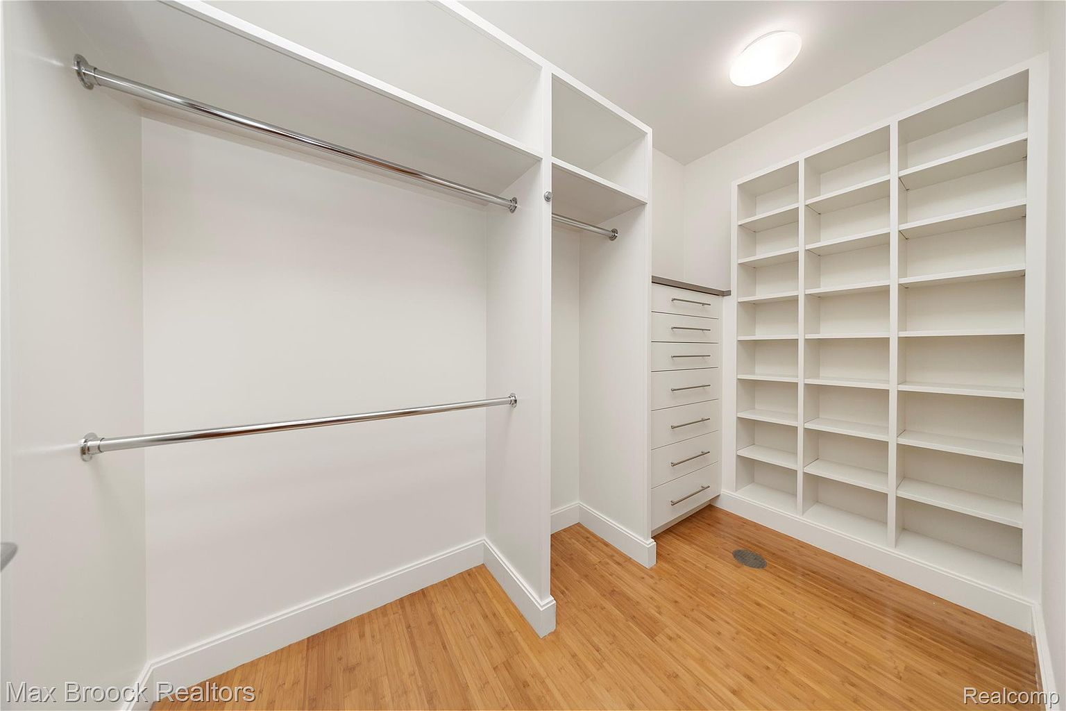 This is a well-organized walk-in closet featuring white shelving and drawers. The closet includes multiple chrome rods for hanging clothes and adjustable shelves for storage. The light wood flooring and bright lighting create a clean and inviting space, perfect for showcasing the storage capacity of the home.