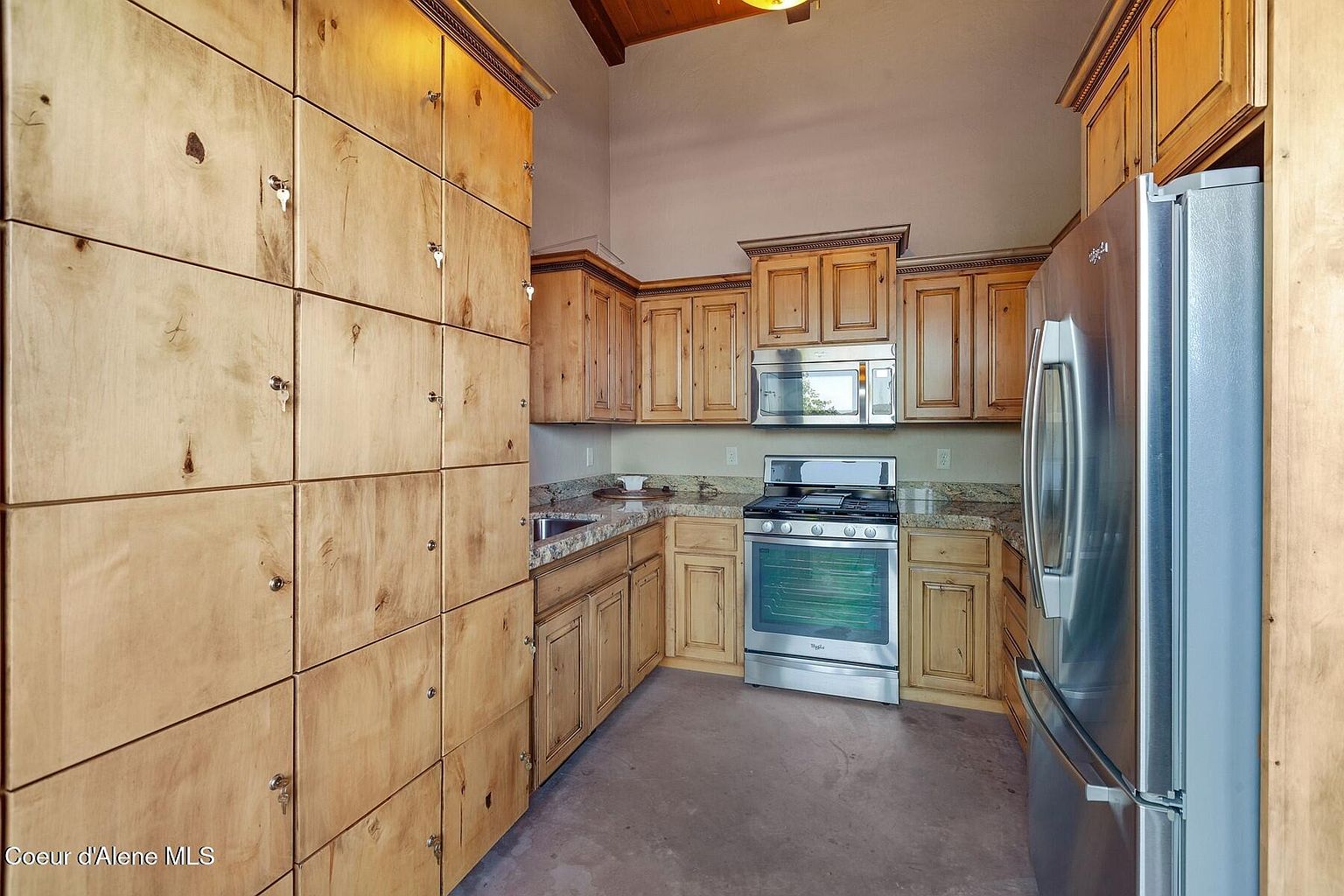 This is a kitchen with light wood cabinets and stainless steel appliances. The cabinets are plentiful, including a large wall of them on the left. The kitchen has a rustic yet modern feel with a stainless steel oven and microwave.