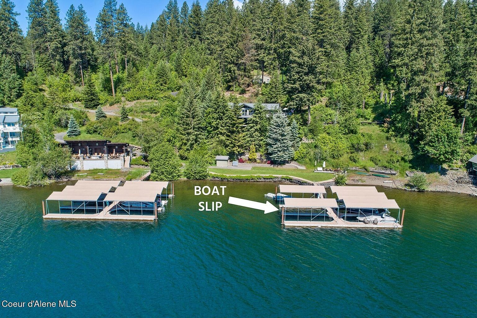 This aerial shot showcases a waterfront property with multiple boat slips. The homes are nestled among lush, mature trees, providing privacy and a scenic backdrop. The calm, deep blue water adds to the property's appeal, suggesting a tranquil and luxurious lifestyle.