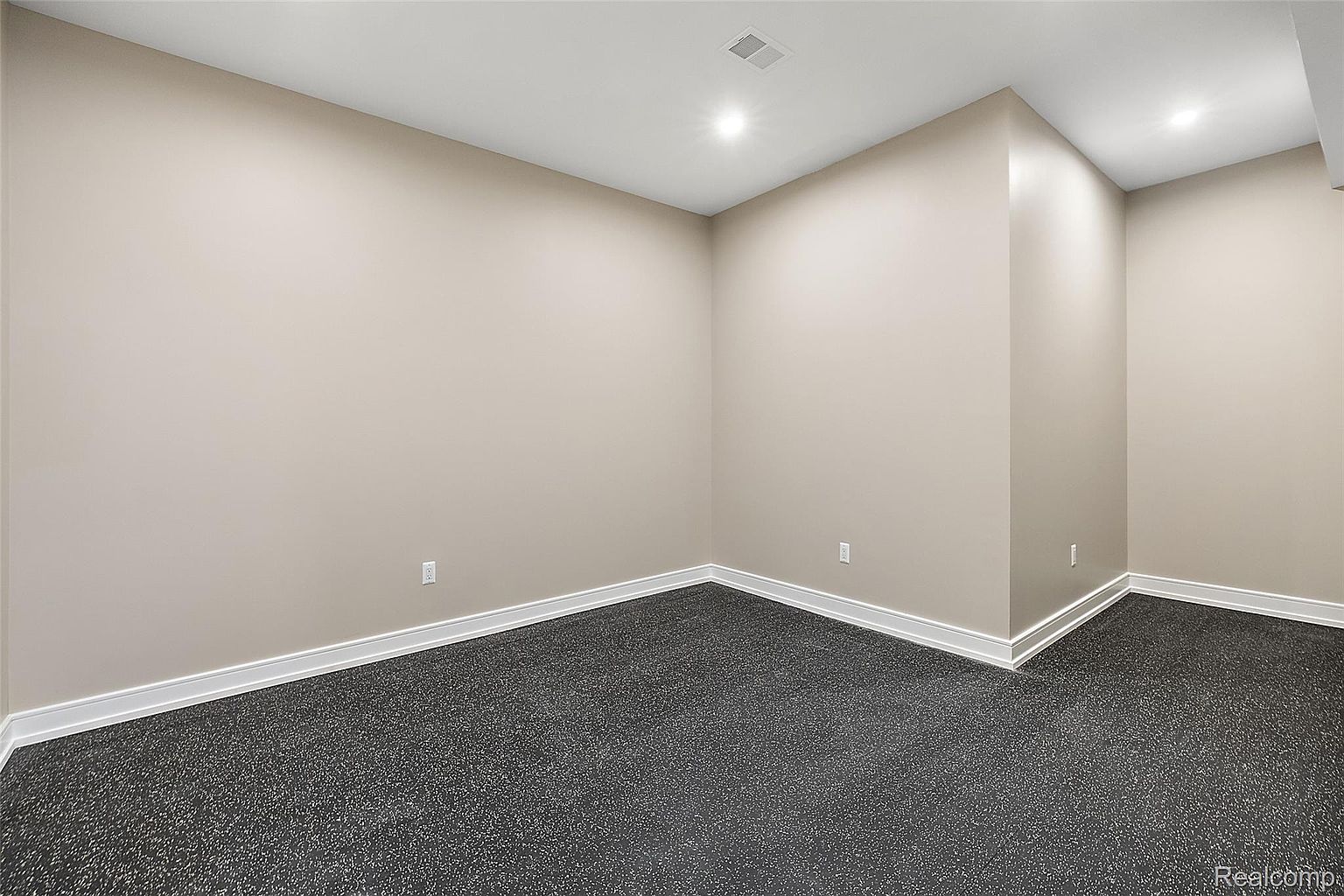 This is an interior shot of a finished basement. The room features neutral-colored walls, white trim, and dark gray carpeting. Recessed lighting provides illumination, and the space appears clean and well-maintained, suggesting a versatile area for recreation or storage.