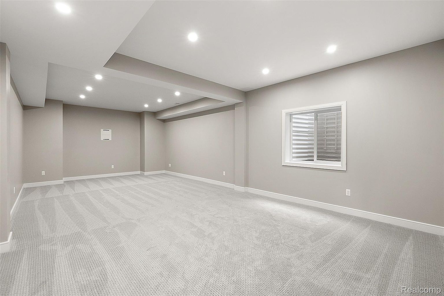 This is a spacious, finished basement featuring neutral-toned walls and light gray carpeting. Recessed lighting provides ample illumination, and a window offers natural light. The room appears clean and well-maintained, suggesting a versatile space for recreation or additional living area.