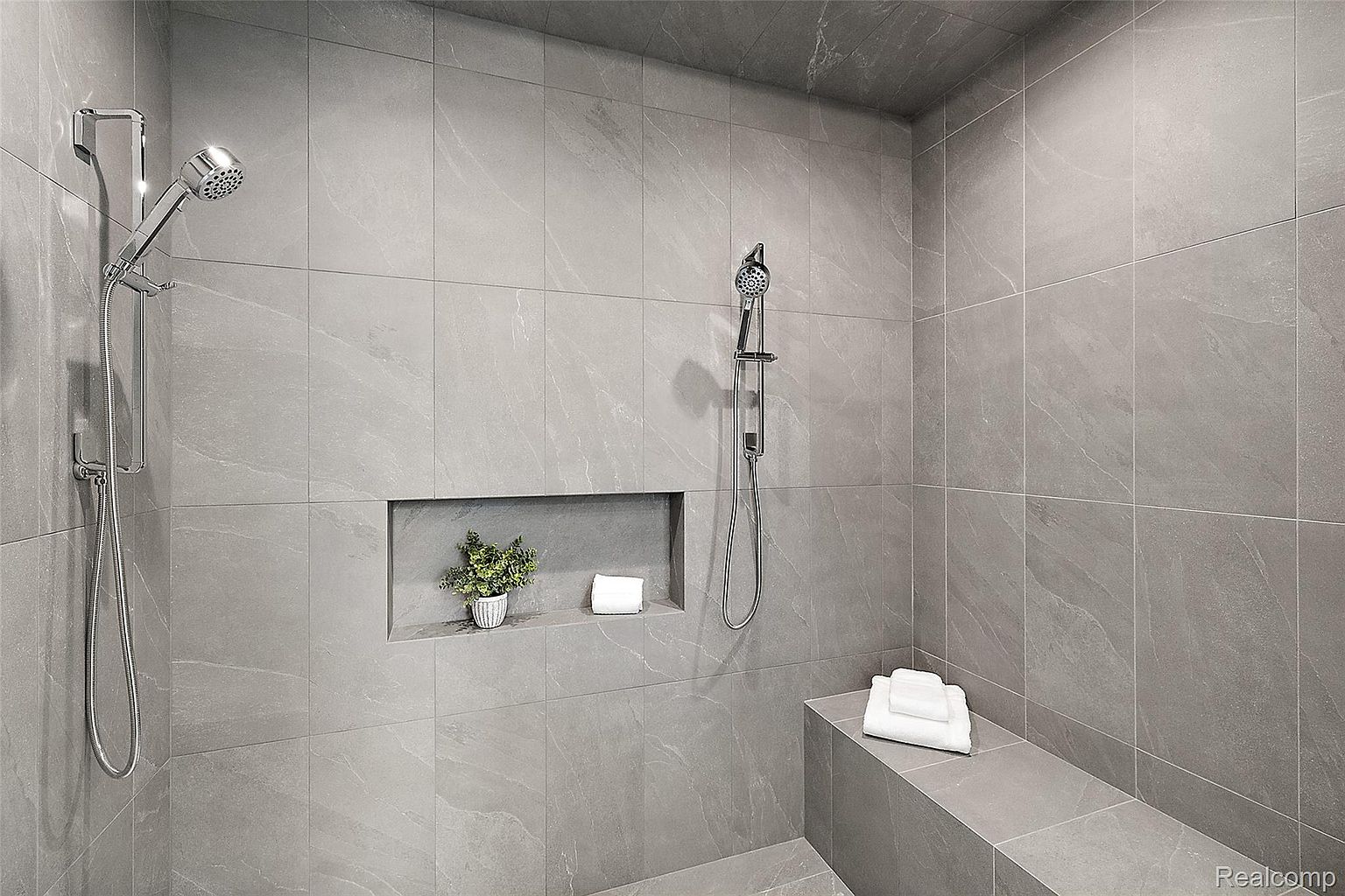 This is a modern primary bathroom featuring a walk-in shower with gray tile walls and a built-in niche for storage. The shower includes both a fixed showerhead and a handheld sprayer. A built-in bench provides seating, and the overall design is sleek and minimalist, creating a spa-like atmosphere.