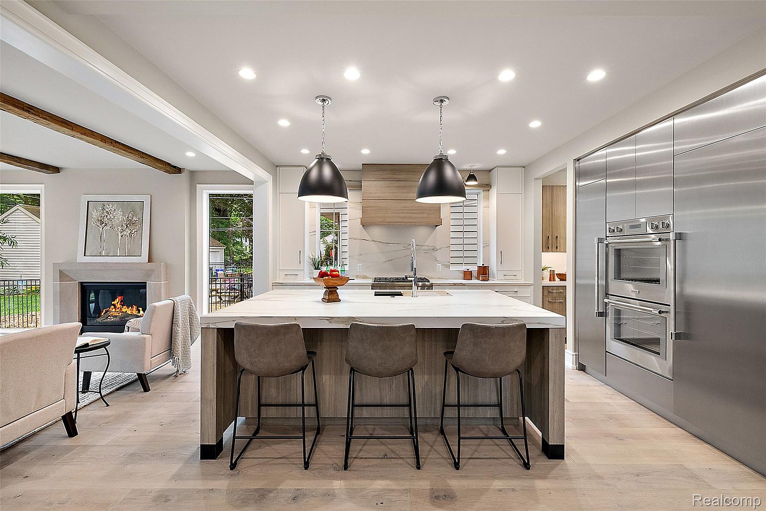 This is a bright and modern kitchen featuring a large island with seating, stainless steel appliances, and custom cabinetry. The open-concept design seamlessly connects to the living area, creating an inviting space for entertaining. Natural light floods the room, highlighting the clean lines and high-end finishes.