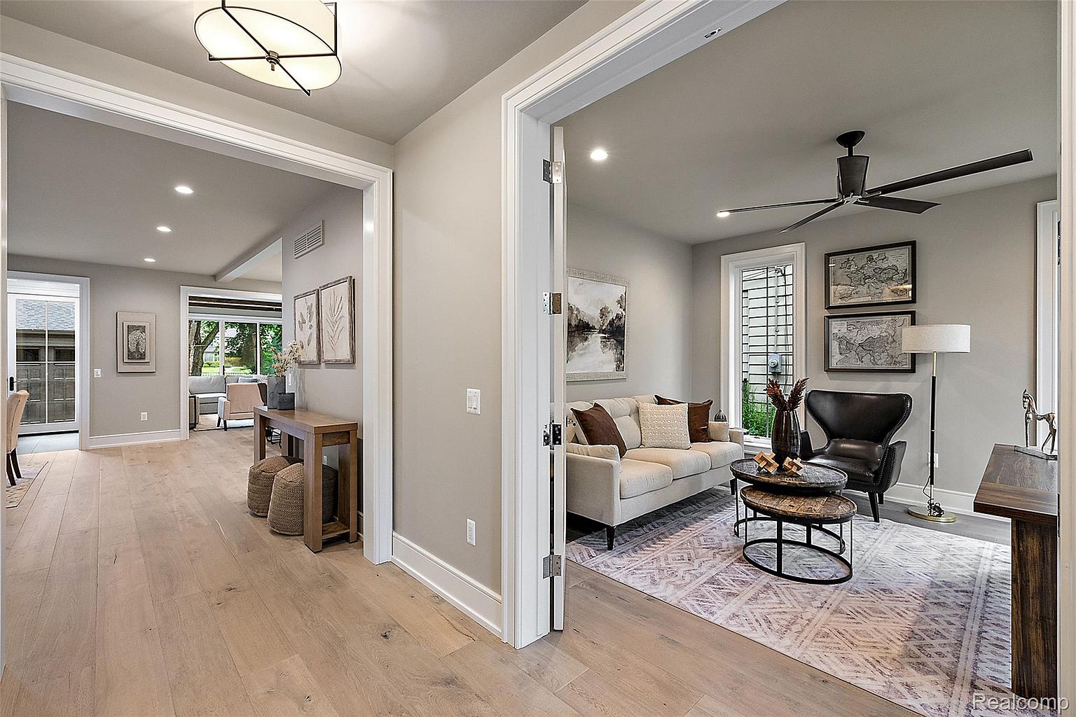 This interior shot showcases a stylish living room with hardwood floors and neutral-toned walls. The space is divided by doorways, offering glimpses into adjacent rooms. A comfortable sofa, accent chair, and decorative rug create an inviting atmosphere, complemented by artwork and modern lighting fixtures.