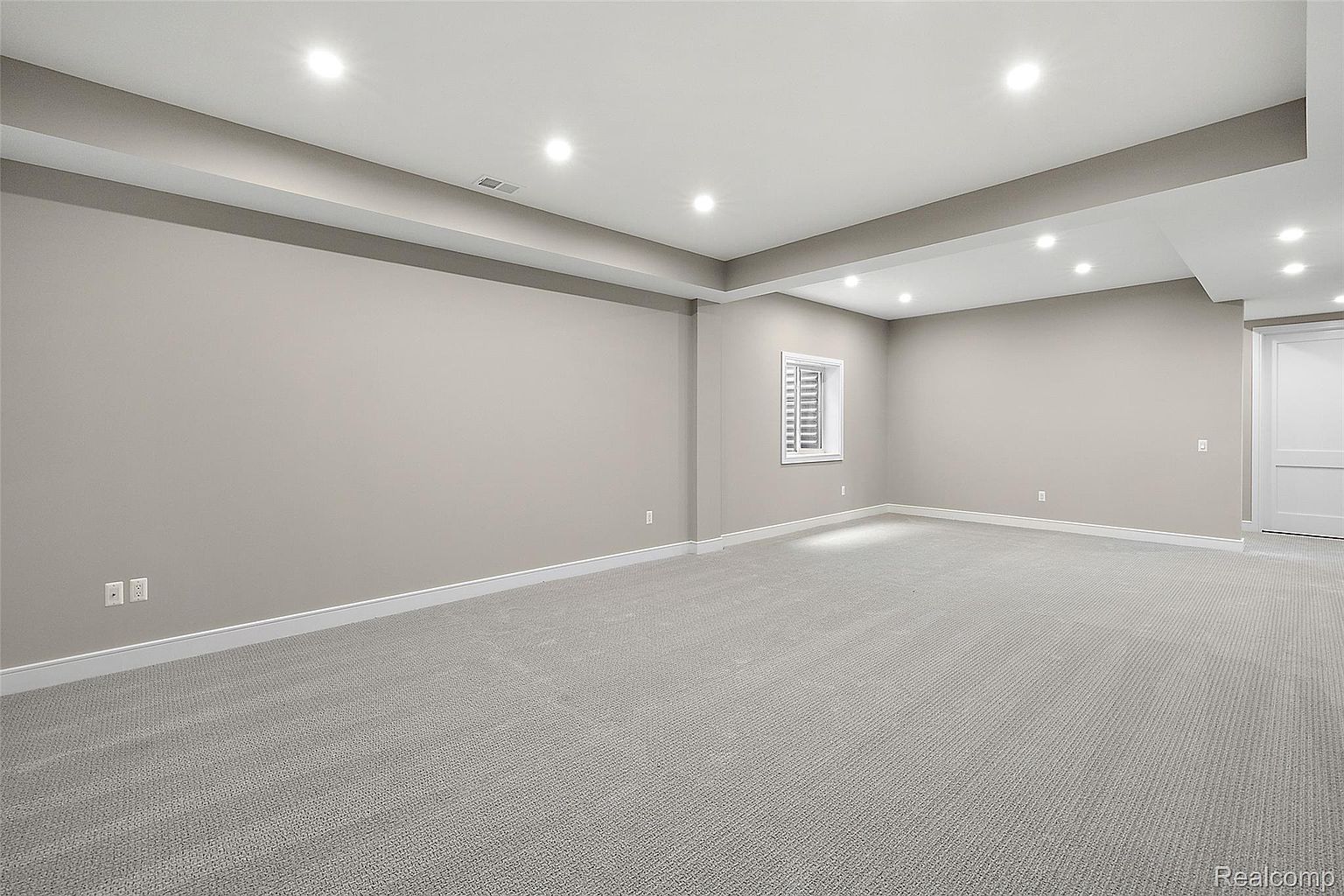 This is a spacious, finished basement featuring neutral-toned walls and carpeting. Recessed lighting provides ample illumination, and a small window offers natural light. The room is clean and appears move-in ready, suggesting a versatile space for recreation or storage.