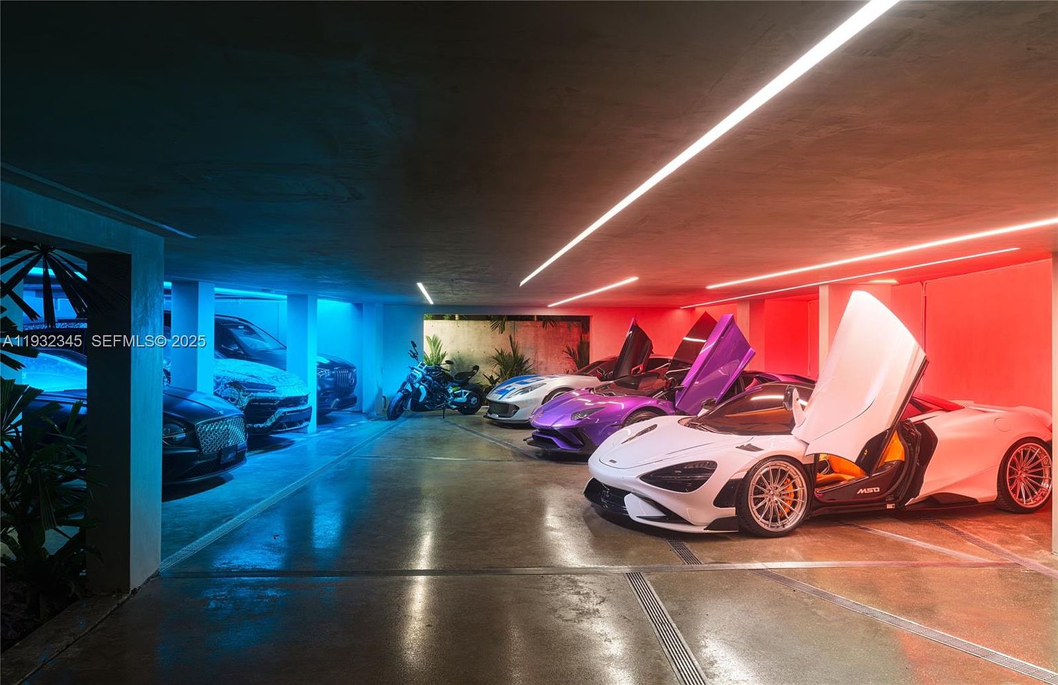 This image showcases a luxurious garage featuring several high-end sports cars and a motorcycle. The garage is illuminated with a modern lighting system that transitions from cool blue to warm red, highlighting the sleek designs of the vehicles. The overall impression is one of opulence and sophistication, perfect for a high-end real estate listing.