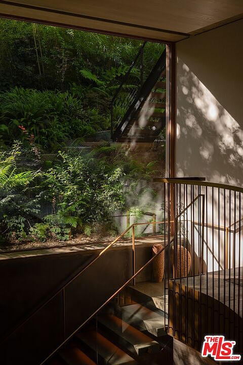 This interior shot showcases a modern staircase with metal railings and wooden steps, bathed in natural light streaming through a large window. The window offers a view of lush greenery, creating a seamless connection between the interior and the surrounding landscape. The design emphasizes clean lines and a minimalist aesthetic, enhancing the sense of tranquility and sophistication.