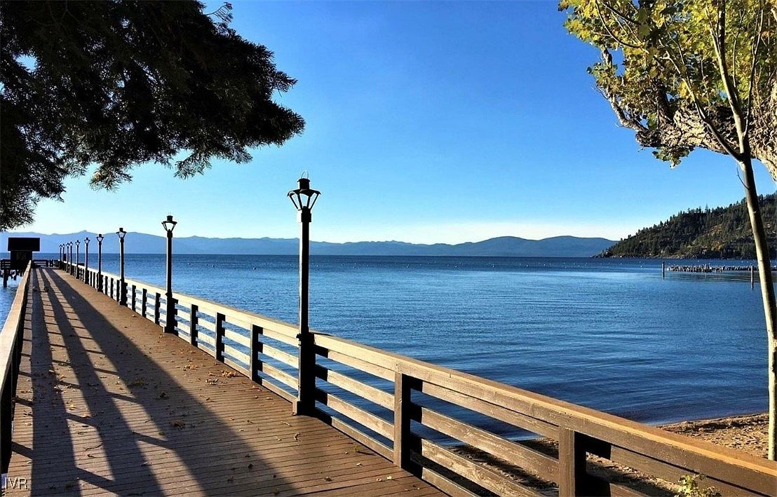 This image showcases a beautiful wooden pier extending into a serene lake under a clear blue sky. The pier is lined with classic lampposts and wooden railings, offering a picturesque view of the water and distant mountains. The scene evokes a sense of tranquility and relaxation, highlighting the property's access to waterfront amenities.