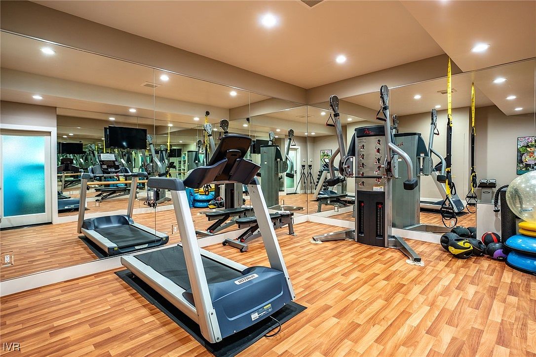 This is a well-equipped home gym featuring a treadmill, a multi-station weight machine, and various exercise accessories. The room has wood-look flooring and mirrored walls that enhance the sense of space. Recessed lighting provides ample illumination, creating a bright and inviting workout environment.