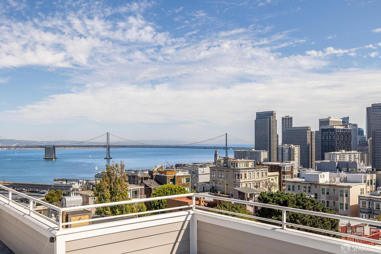 This image showcases a stunning view from a patio or balcony, overlooking a cityscape with a prominent bridge in the background. The railing of the patio is visible in the foreground, providing a sense of enclosure and perspective. The overall impression is one of luxury and breathtaking urban living.