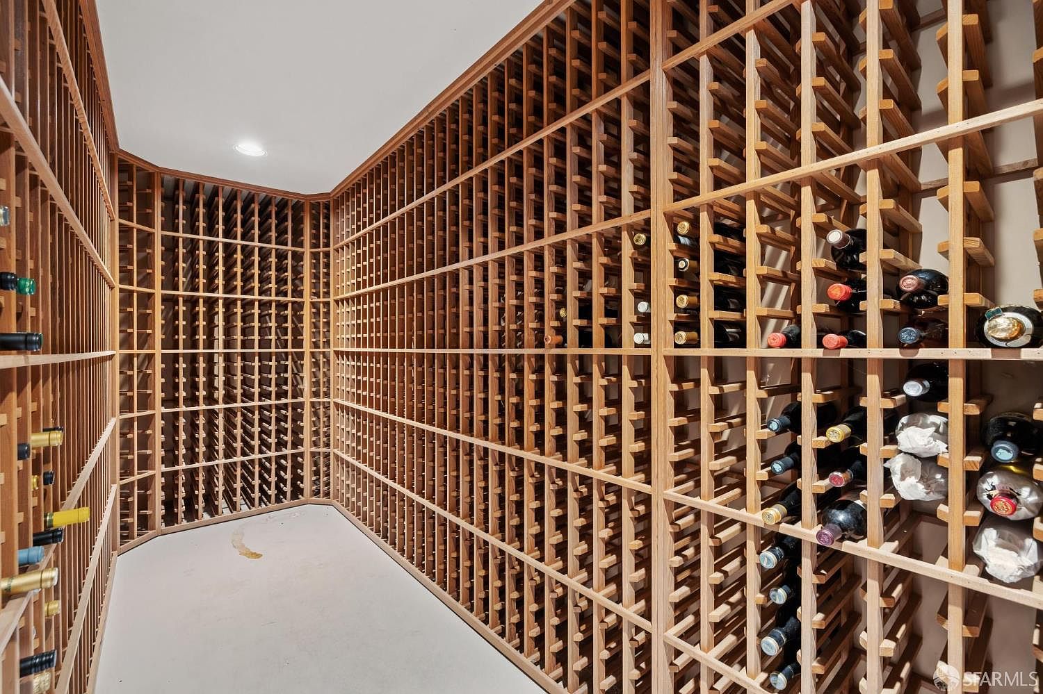 This is an interior shot of a well-stocked wine cellar. The cellar features extensive wooden racking systems filled with numerous wine bottles. The room is brightly lit, showcasing the organized and spacious storage for wine enthusiasts.