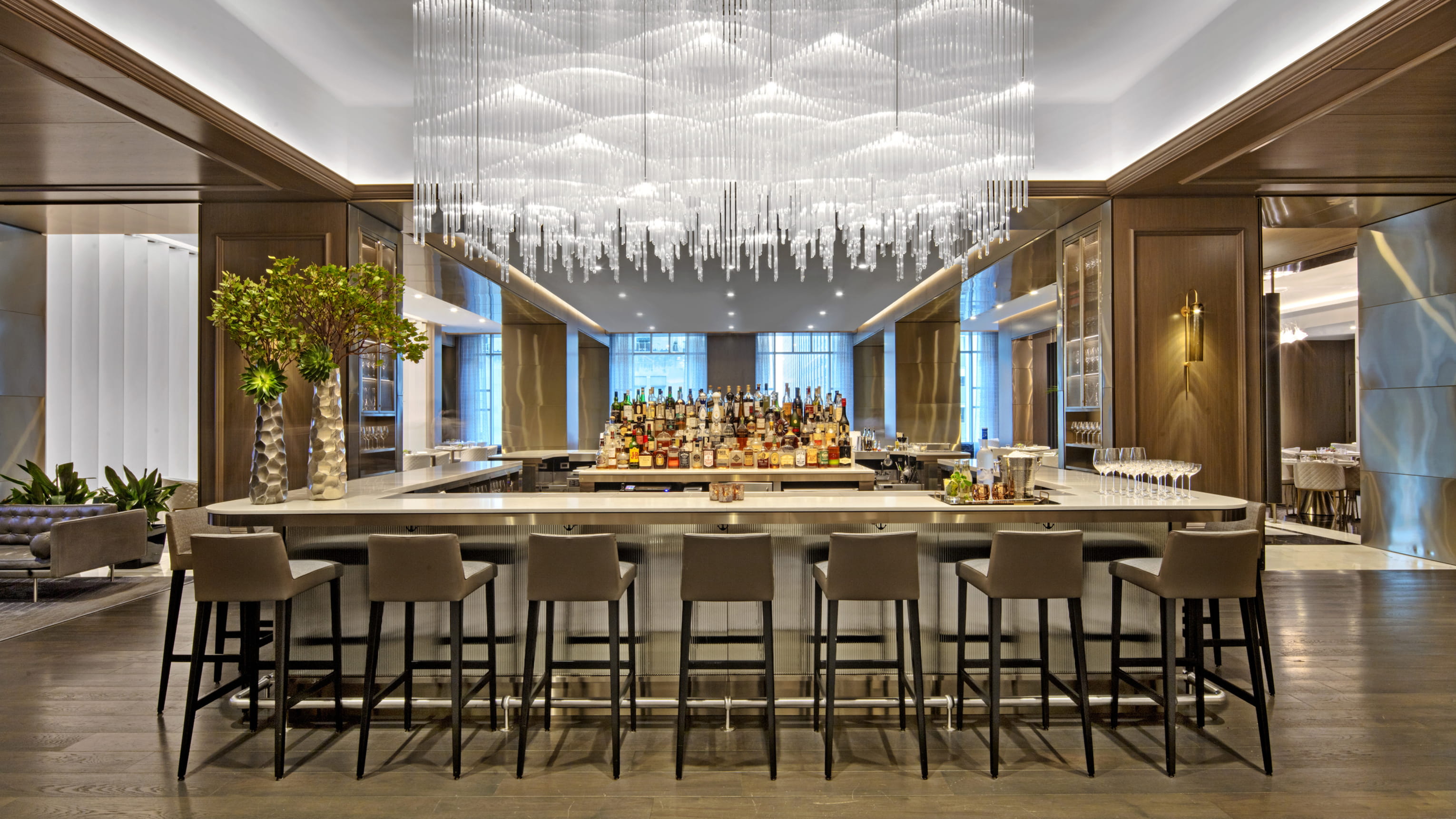 This image showcases a well-appointed bar area. The focal point is the expansive bar counter with multiple stools, complemented by a decorative glass-rod chandelier. The bar is fully stocked with a wide assortment of beverages, creating an inviting and luxurious ambiance perfect for entertaining.