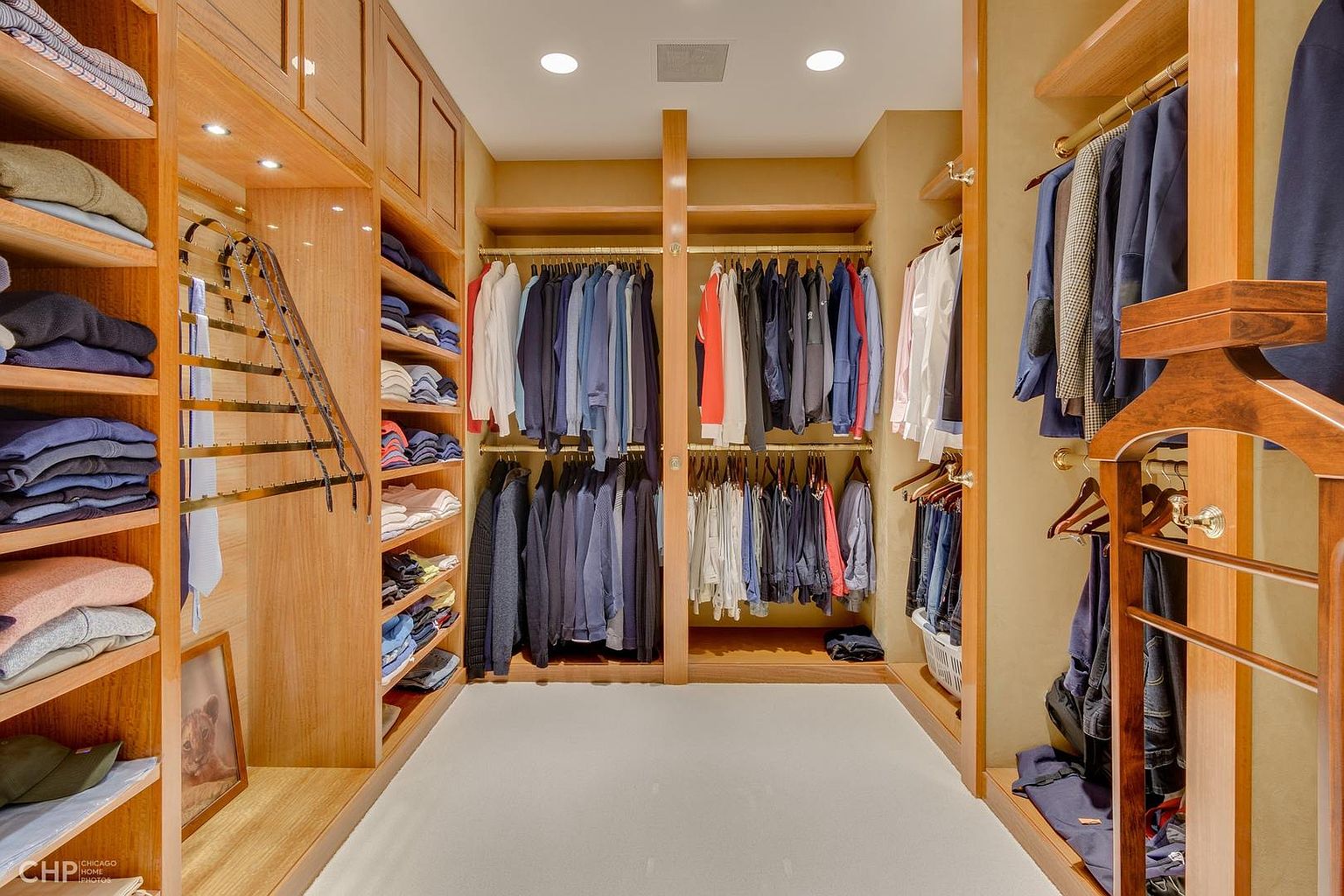 This is a well-organized walk-in closet featuring custom wooden shelving and hanging rods. Clothes are neatly arranged, showcasing ample storage space. The closet is brightly lit, creating a luxurious and functional space.