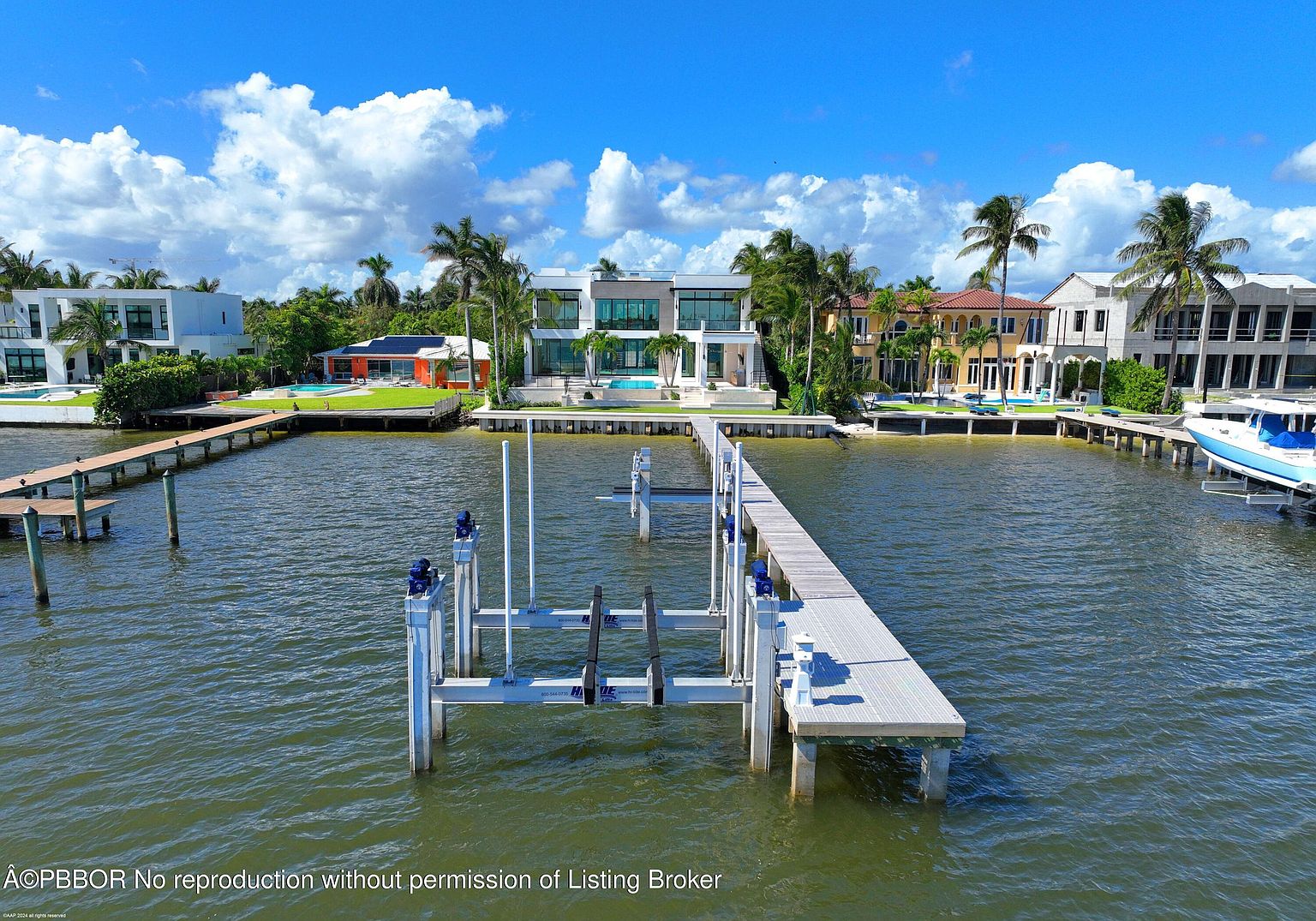 This aerial view showcases waterfront properties with modern architectural designs, featuring private docks and boat lifts. The properties are lined with palm trees and well-maintained landscaping, creating a luxurious and serene atmosphere. The clear blue sky and calm water enhance the overall appeal, emphasizing the desirable waterfront lifestyle.