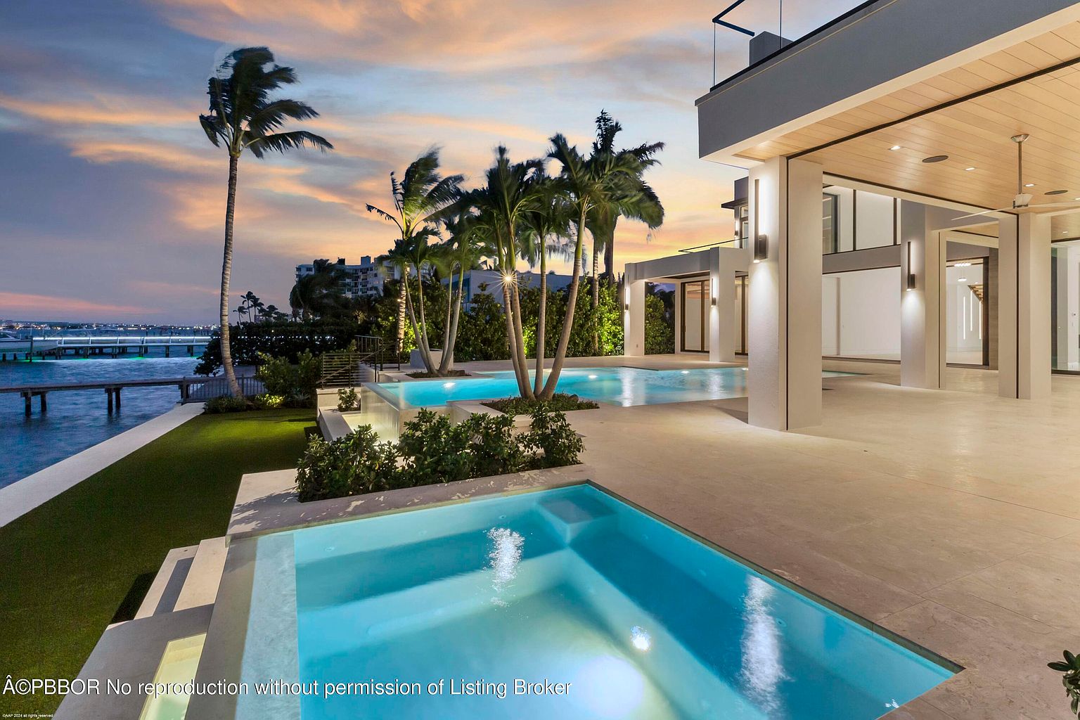 This image showcases a luxurious backyard with multiple pools and a modern architectural design. Palm trees sway gently in the background, complementing the sleek lines of the house and the inviting turquoise water of the pools. The scene is bathed in the warm light of dusk, creating an atmosphere of relaxation and upscale living.