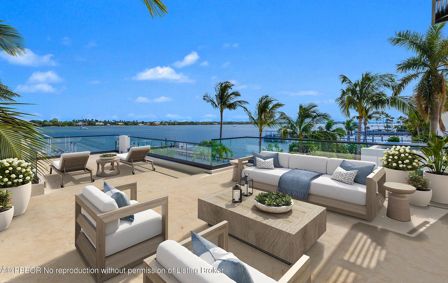 This image showcases a luxurious outdoor patio or deck area with stylish furniture, including a sofa, chairs, and lounge chairs, all arranged to maximize the stunning waterfront view. The space is adorned with potted plants and decorative elements, creating an inviting and upscale atmosphere. The clear glass railing ensures an unobstructed view of the water and surrounding landscape, enhancing the property's appeal.