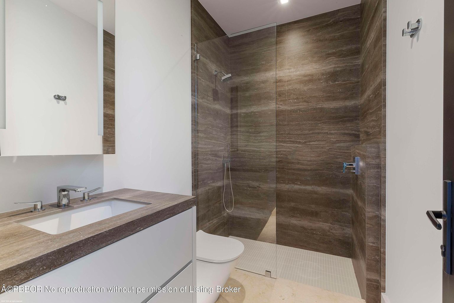 This is a modern bathroom featuring a floating vanity with a stone countertop and a rectangular sink. The shower has a glass enclosure and is tiled with horizontal brown stone, complemented by a white tiled floor. The overall design is sleek and minimalist.