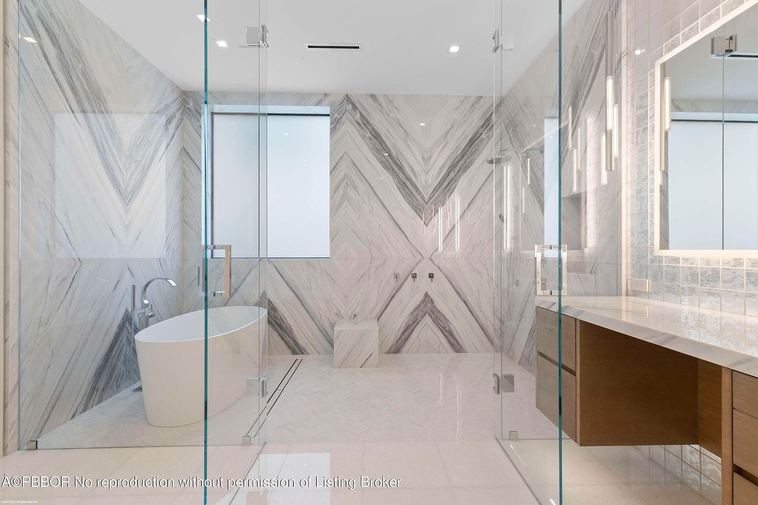This is a luxurious primary bathroom featuring a freestanding soaking tub with a modern faucet, enclosed by a frameless glass shower. The walls are adorned with chevron-patterned marble tiles, complemented by herringbone-patterned floor tiles. A sleek vanity with wood cabinetry and a marble countertop is visible, along with modern pendant lighting and a large mirror, creating a spa-like atmosphere.