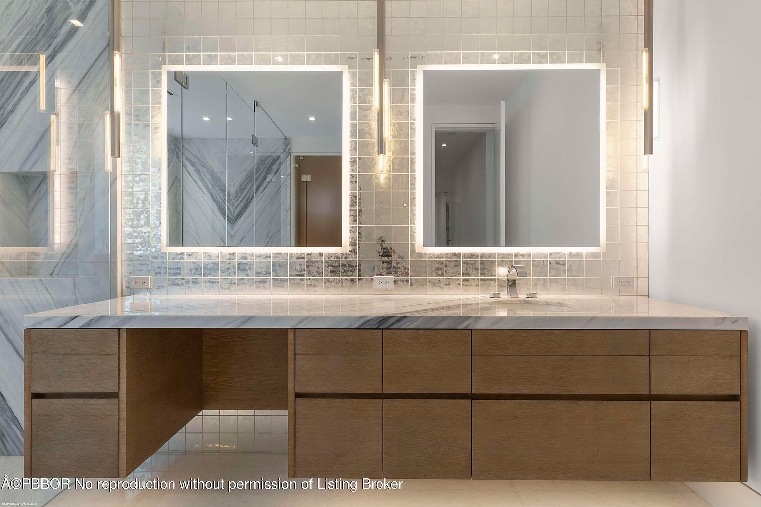This is a well-lit primary bathroom featuring a double vanity with a marble countertop and wooden cabinets. Two square, illuminated mirrors hang above the sinks, complemented by modern light fixtures. The backsplash is tiled, adding texture and visual interest to the space, creating a luxurious and functional area.