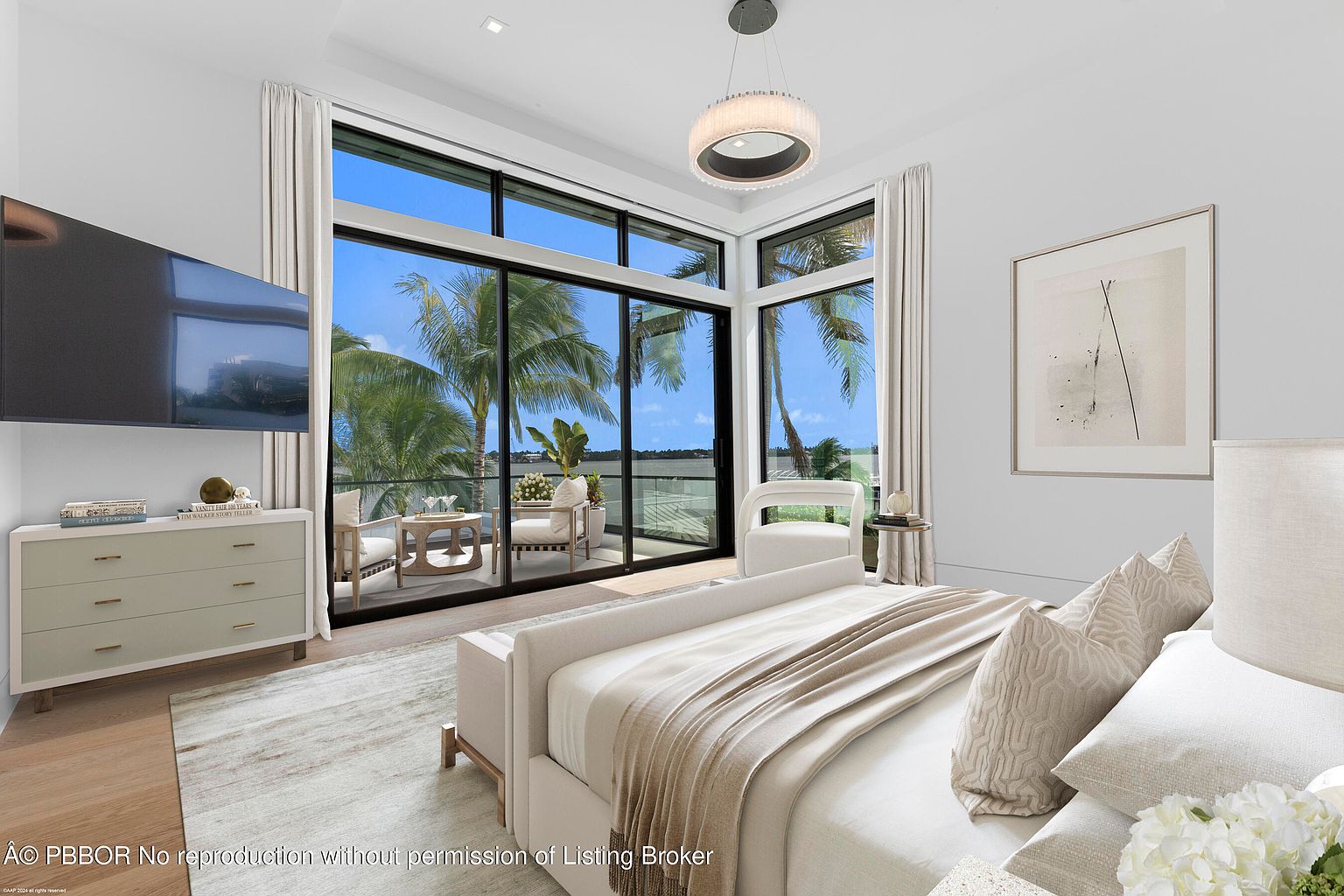 This is a bright and airy primary bedroom featuring a large window with a view of palm trees and water. The room is decorated in neutral tones with a light-colored bed, a dresser with a TV above it, and a modern chandelier. The overall impression is luxurious and serene, highlighting the waterfront location.