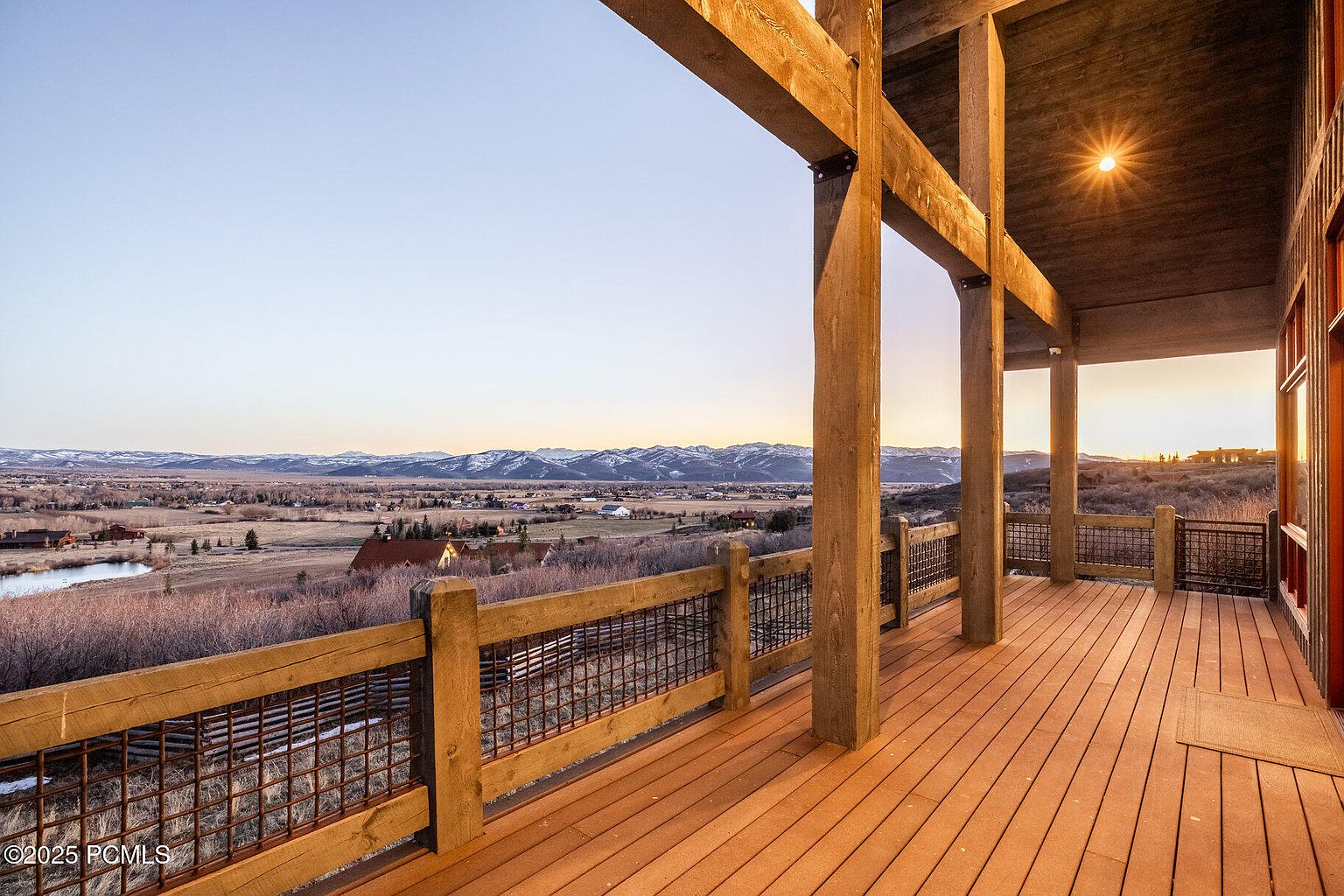 This image showcases a spacious wooden deck with a rustic yet modern design. The deck features sturdy wooden beams and railings with metal mesh inserts, offering a secure and stylish enclosure. The view extends over a picturesque landscape with mountains in the distance, creating a serene and inviting outdoor living space.