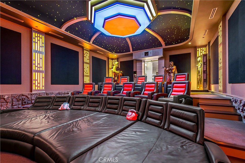 This highly themed Star Wars-inspired home theater features a tiered seating arrangement with plush leather recliners and a large, curved front lounge area. The room is decorated with life-sized character statues, custom wall paneling, and a dramatic ceiling design that mimics a starry night sky with a central geometric light fixture. The overall impression is an immersive, luxury entertainment space designed for a dedicated fan.