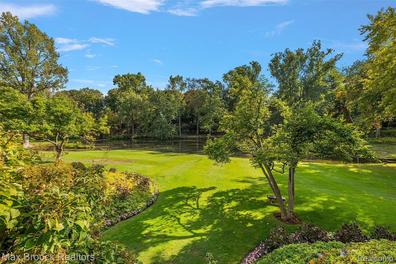 This image showcases a meticulously maintained yard or garden, featuring lush green grass, mature trees, and carefully arranged flower beds. A small pond or water feature adds to the serene atmosphere. The scene evokes a sense of tranquility and natural beauty, highlighting the property's outdoor appeal.