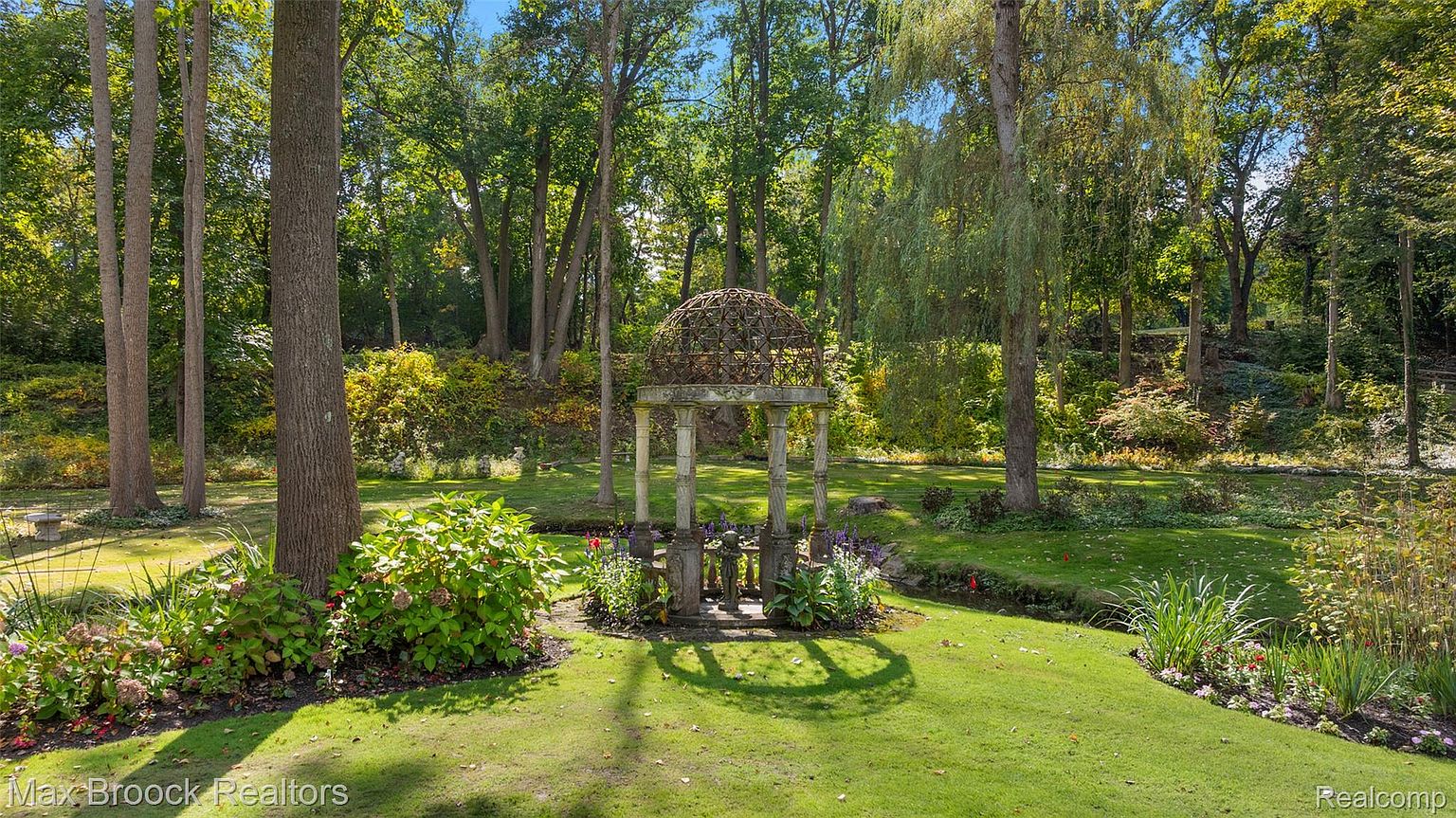 This image showcases a beautifully landscaped garden with a charming gazebo as its focal point. Lush green grass, mature trees, and colorful flowerbeds create a serene and inviting outdoor space. The scene evokes a sense of tranquility and privacy, making it an ideal setting for relaxation and outdoor enjoyment.