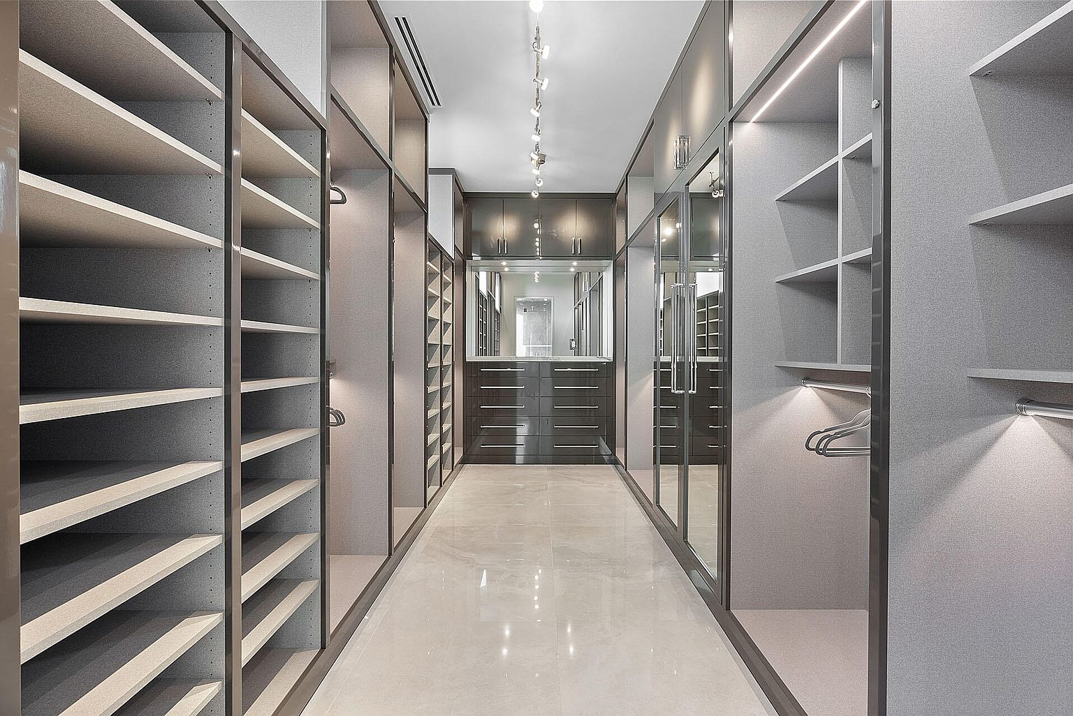 This is a well-organized and luxurious walk-in closet. The closet features custom shelving, drawers, and hanging rods, providing ample storage space. The lighting is strategically placed to highlight the closet's features, and the overall design is sleek and modern, creating a sophisticated and functional space.
