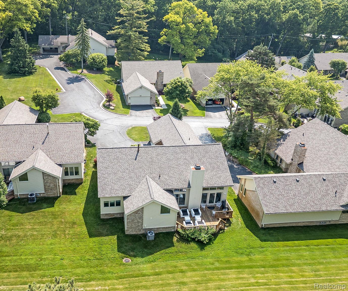 This aerial shot showcases a residential neighborhood with well-maintained lawns and mature trees. Several houses with varying rooflines and architectural details are visible, each featuring a deck or patio area. The overall impression is one of a peaceful and established community.