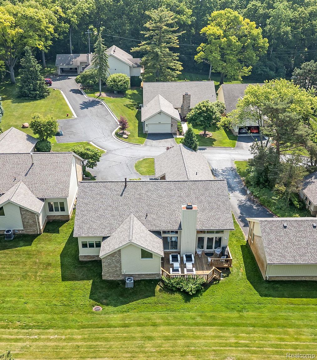 This aerial shot showcases a residential neighborhood with well-maintained lawns and mature trees. Several houses with varying rooflines and architectural details are visible, connected by paved driveways and roads. The overall impression is one of a peaceful and established community.