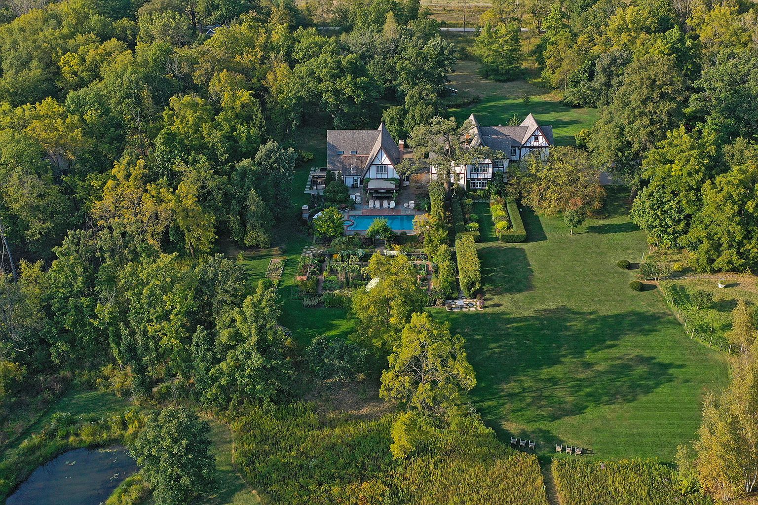 This aerial shot showcases a sprawling estate nestled among lush greenery. The Tudor-style home features a swimming pool, manicured gardens, and expansive lawns. The property exudes a sense of privacy and luxury, making it an ideal retreat.