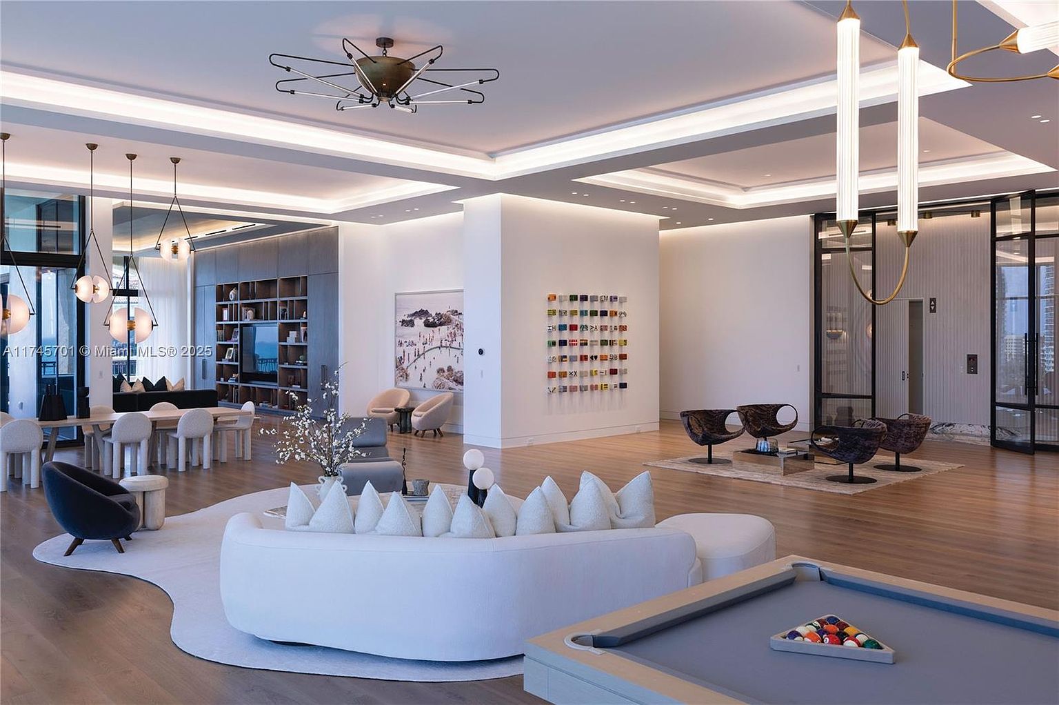 This image showcases a luxurious community amenity space, featuring a modern design with a blend of seating areas, including a curved sofa and stylish chairs. The space is well-lit with contemporary lighting fixtures and includes a pool table, suggesting a recreational area for residents. The overall impression is one of sophistication and comfort, designed for relaxation and social interaction.
