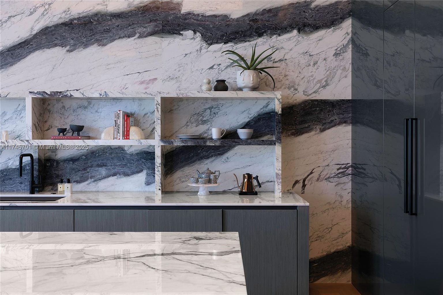 This image showcases a modern kitchen with a striking marble backsplash and countertop, complemented by sleek gray cabinetry. Open shelving displays decorative items, adding a touch of personality to the space. The overall design exudes luxury and sophistication, making it an appealing feature for potential buyers.